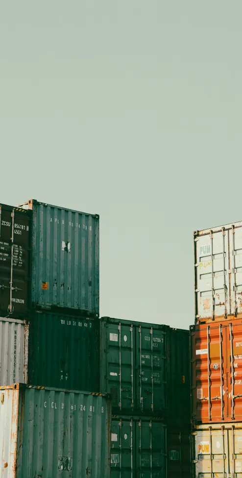 Stacked shipping containers in green and orange at a terminal yard