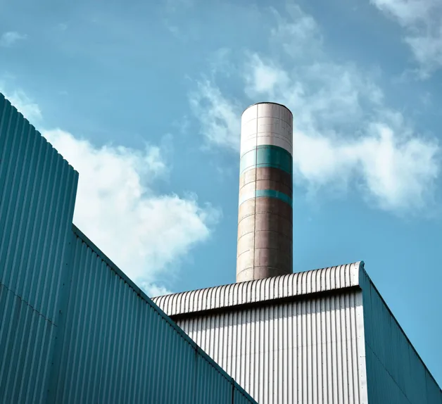 A banded chimney rising above a corrugated industrial plant